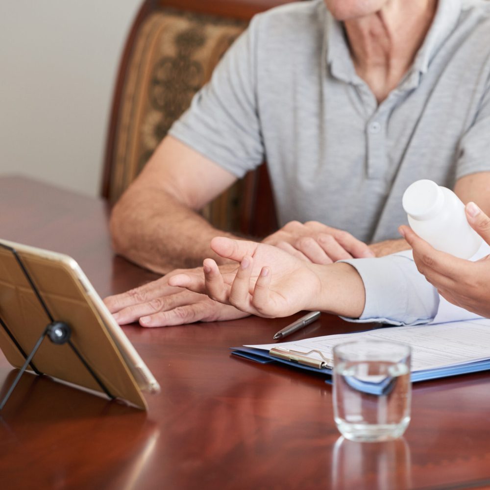 Faceless shot of doctor showing tablet to senior patient while promoting pills at table